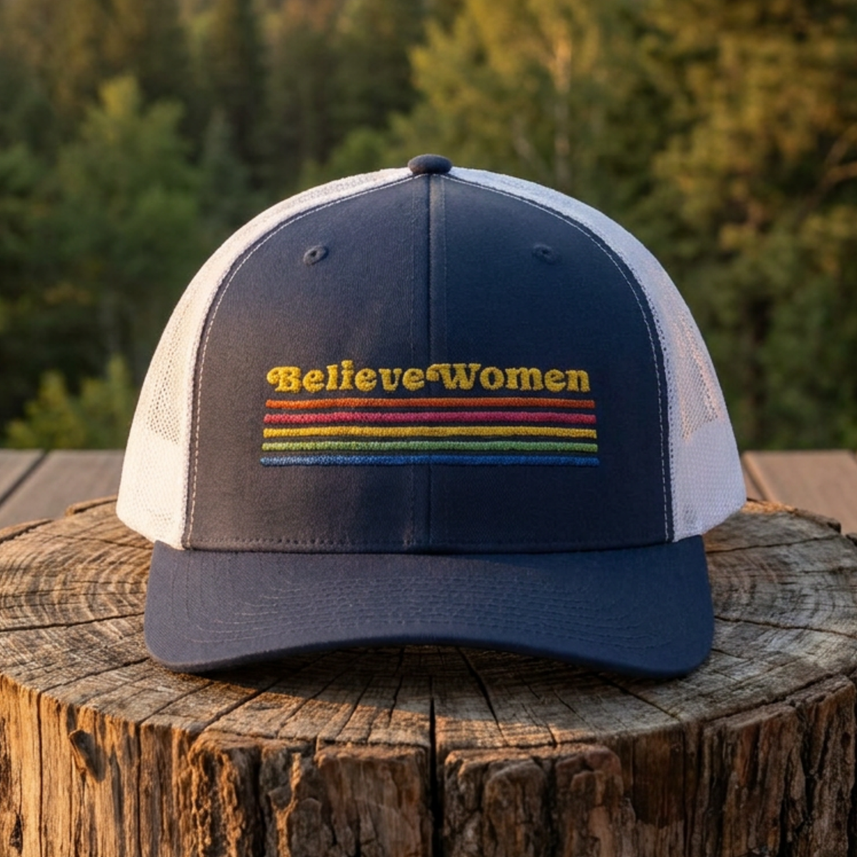 Believe Women embroidered feminist trucker hat with rainbow stripe detail, structured front, breathable mesh back, and adjustable snap closure.