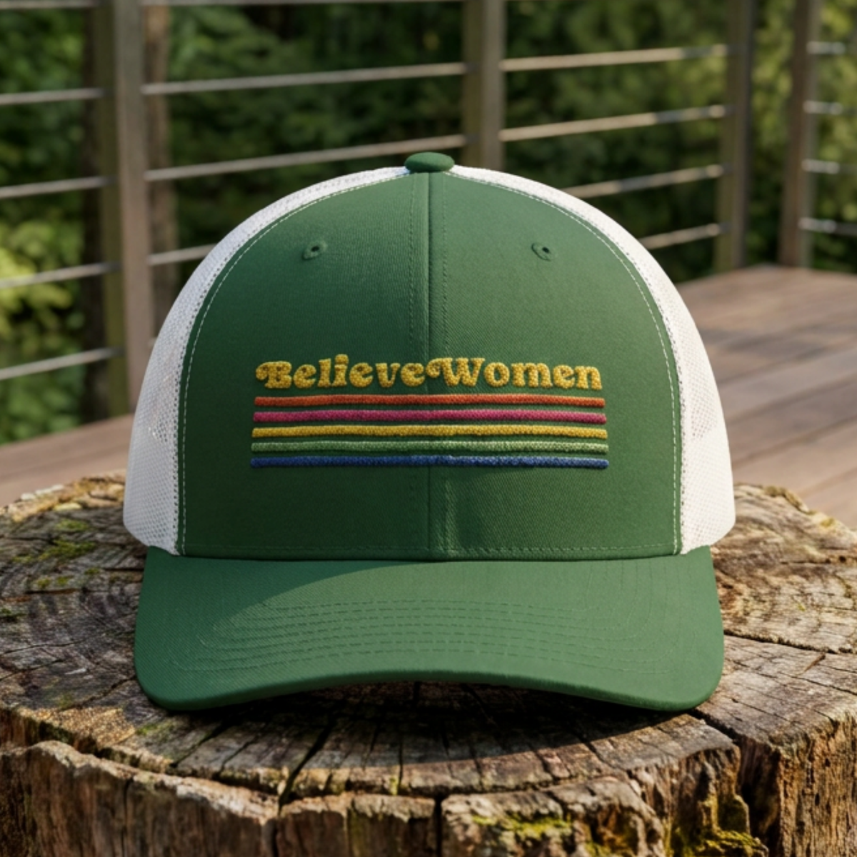 Believe Women embroidered feminist trucker hat with rainbow stripe detail, structured front, breathable mesh back, and adjustable snap closure.