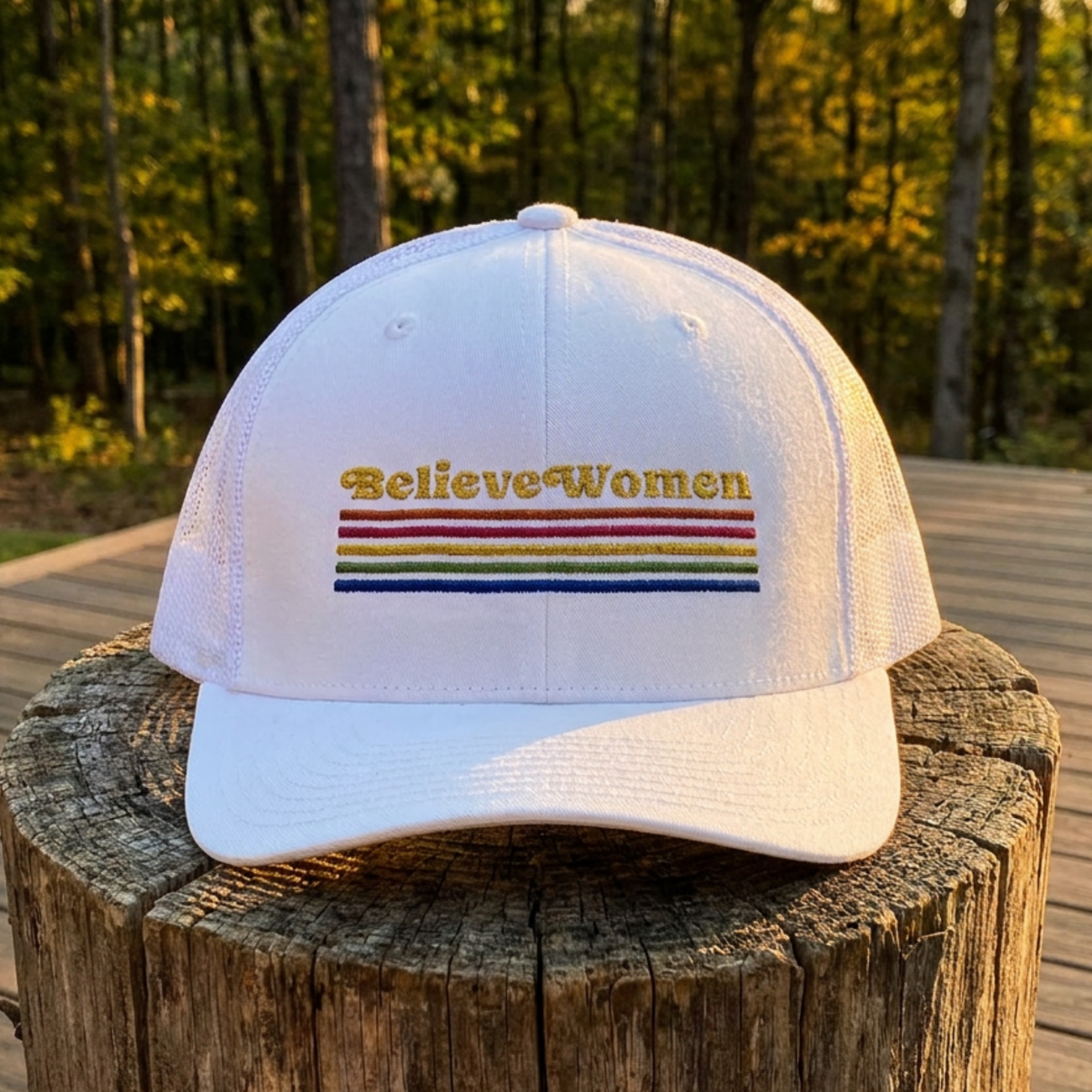 Believe Women embroidered feminist trucker hat with rainbow stripe detail, structured front, breathable mesh back, and adjustable snap closure.